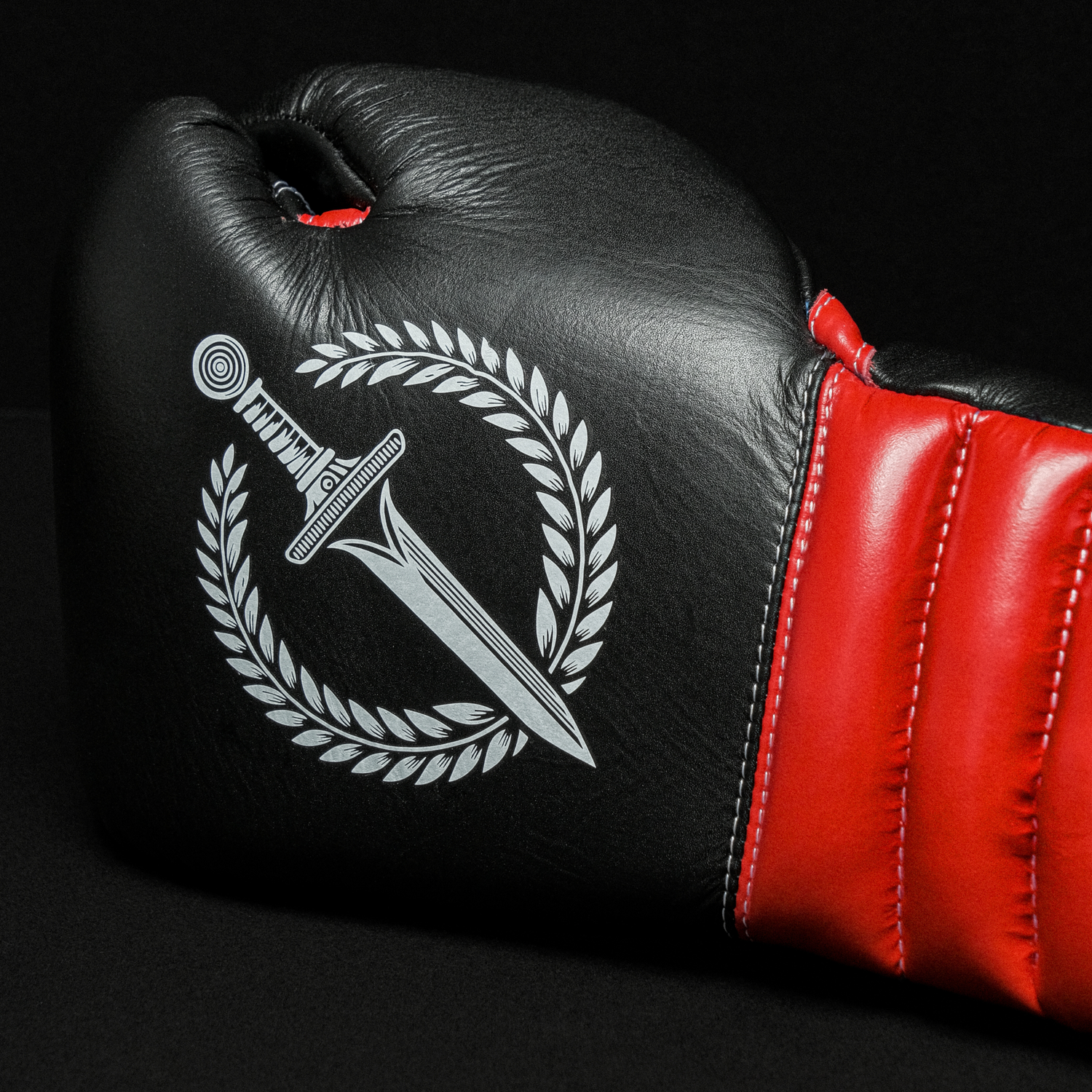 Black boxing glove with a red accent featuring a white emblem on a black background
