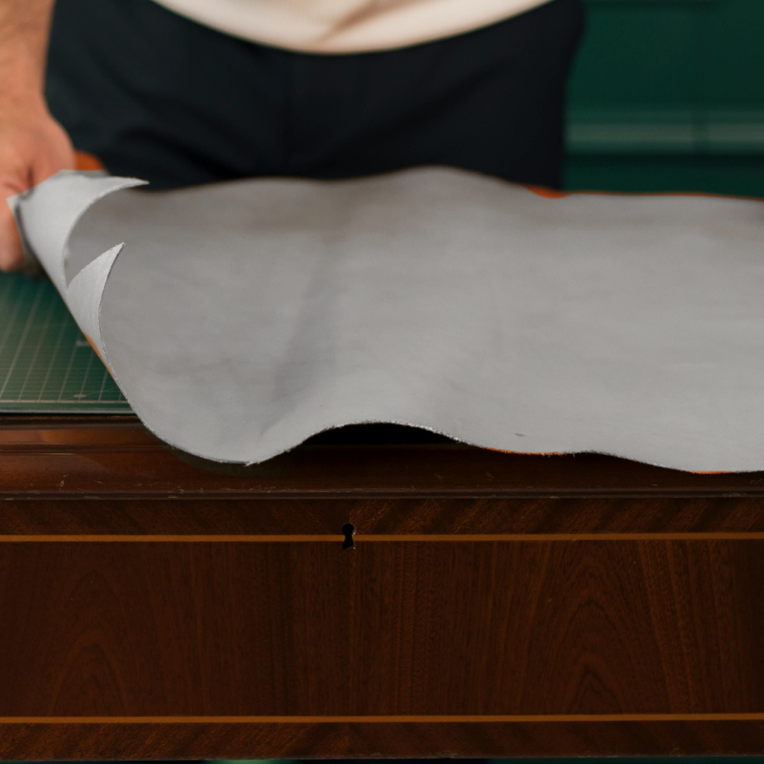 Person rolling out a large sheet of white leather on a wooden surface.