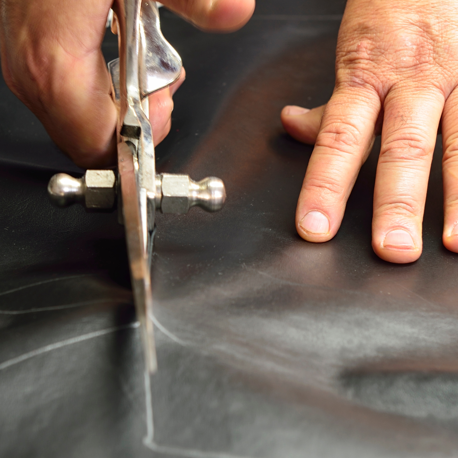Close-up of hands using a tool on a dark surface.