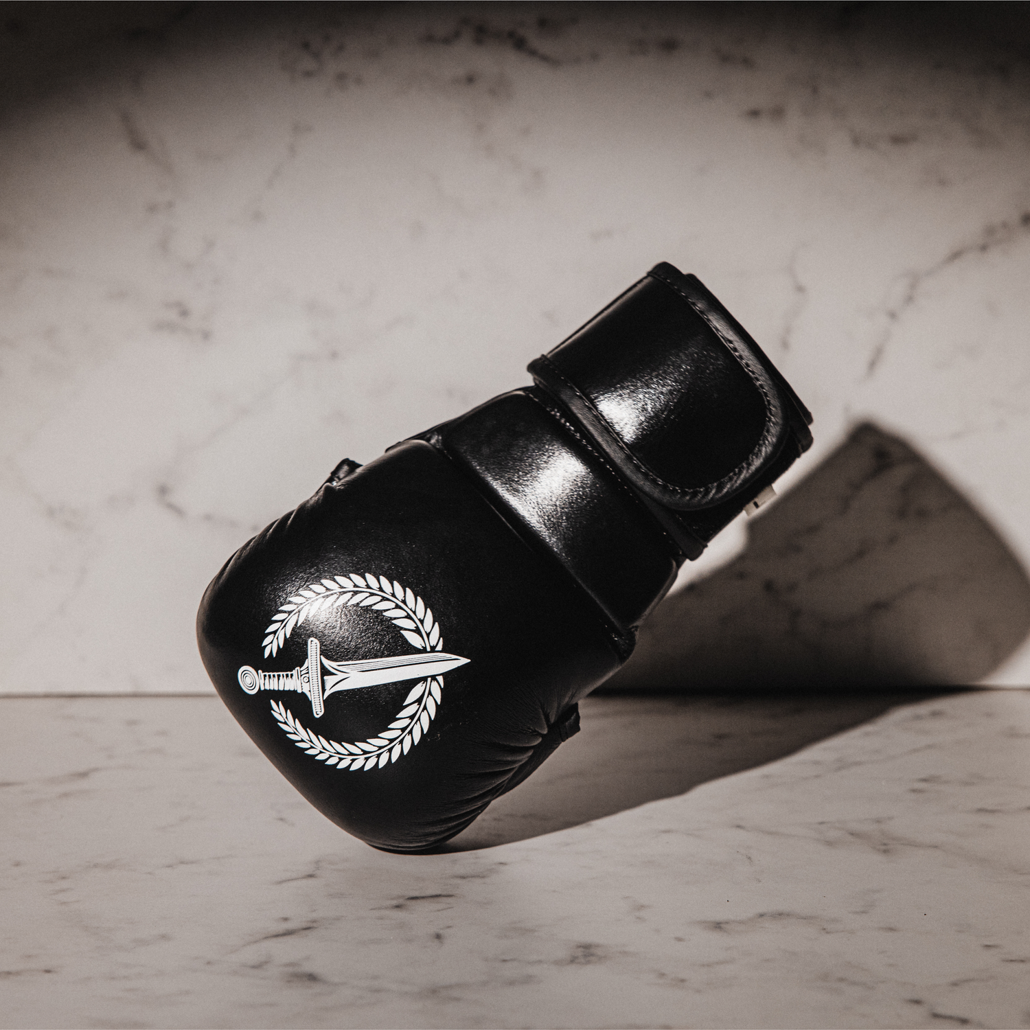 Black MMA glove with a logo on a marble surface.