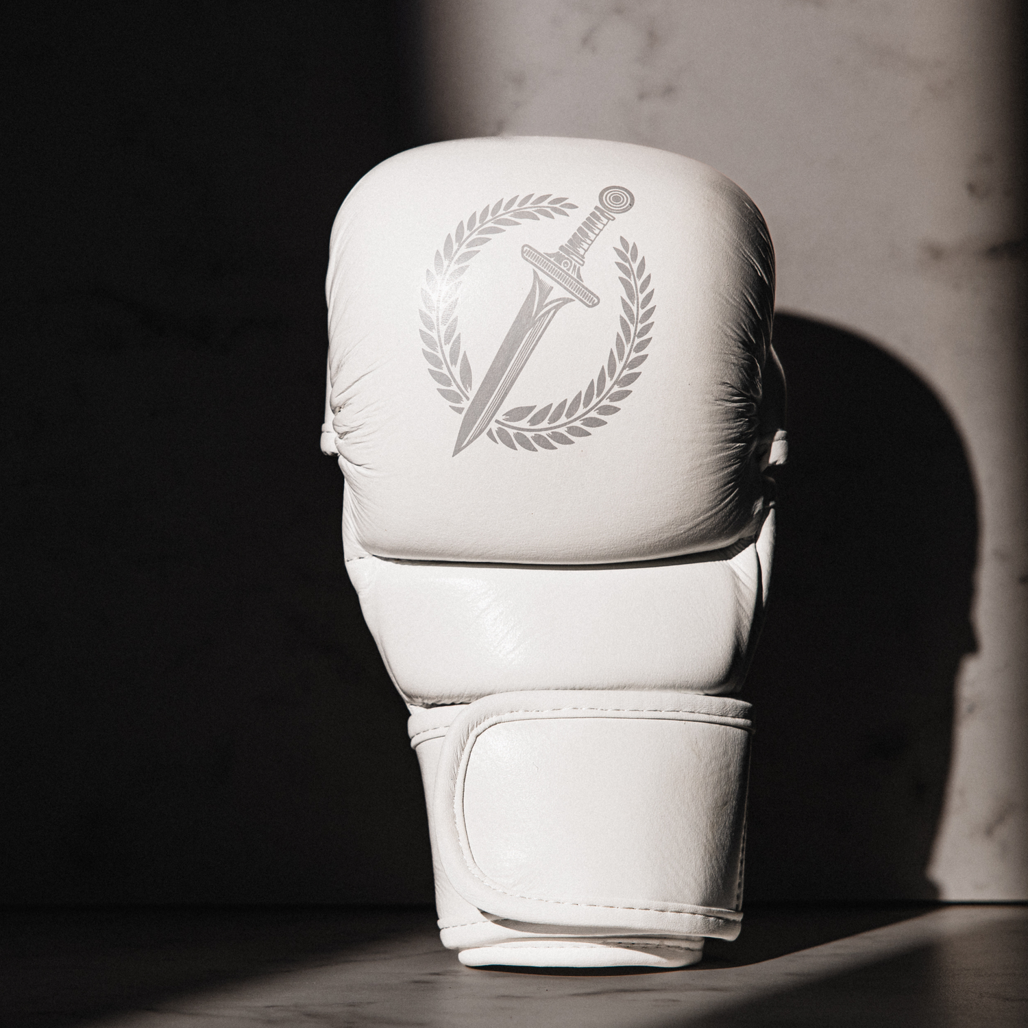White MMA glove with a logo on a dark surface.