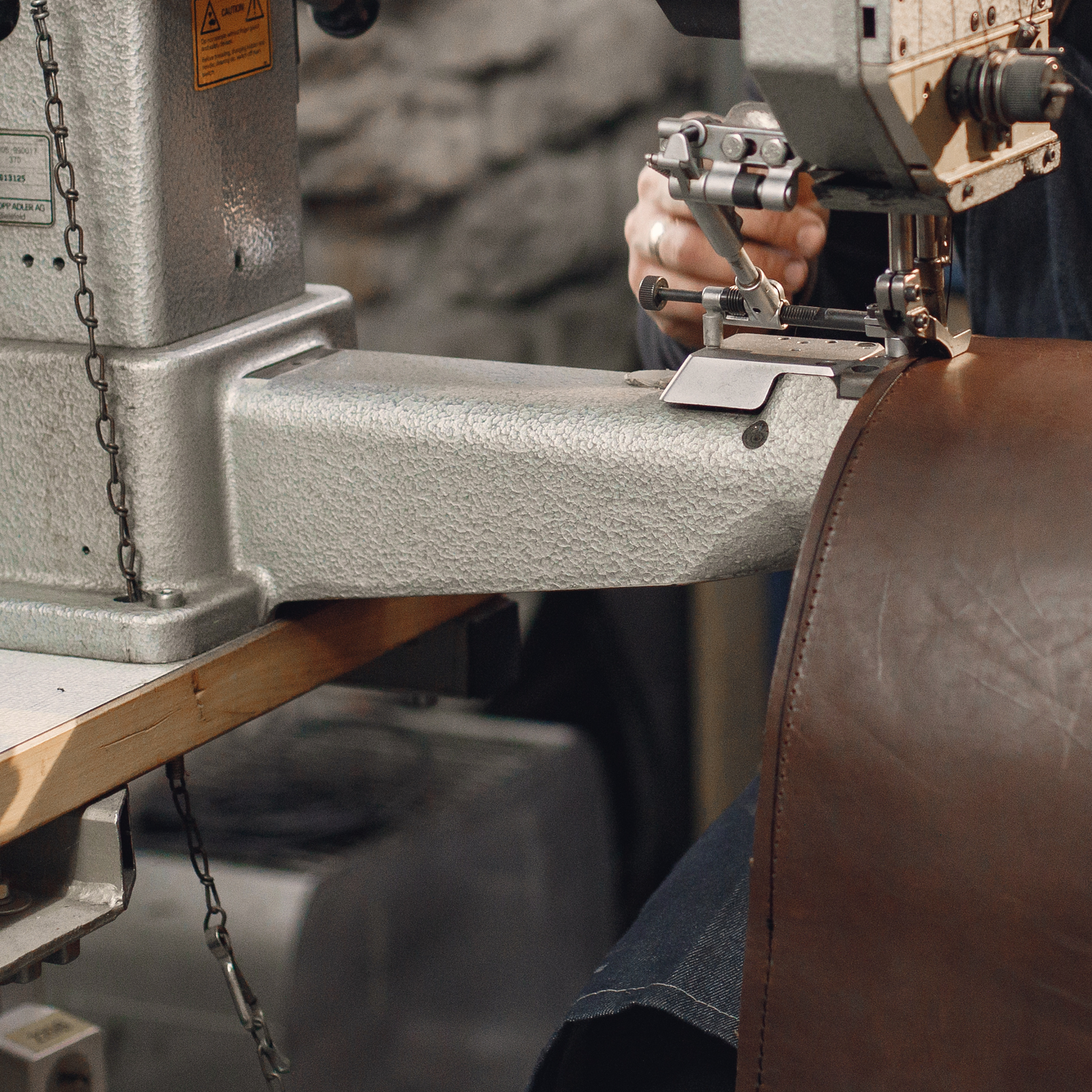 Person operating a leather sewing machine with a blurred background.